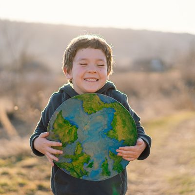 Junge hält Weltkugel in den Händen vor Feld im Frühling